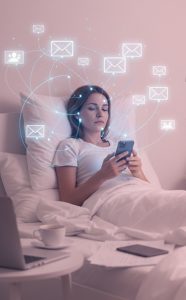 Krupni plan žene koja leži u krevetu odmah nakon buđenja, držeći telefon u ruci u polumraku sobe. Iznad njene glave lebdi kompleksna, svetlucava mreža digitalnih ikona (mejlovi, obaveštenja, poruke) koja simbolizuje trenutnu neurološku preopterećenost i reaktivnost.